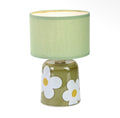 Green table lamp with bold white flower detailing and a simple green fabric shade.