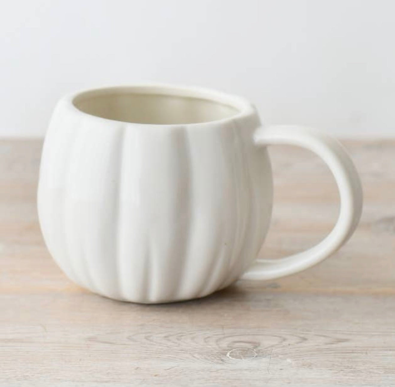 Glossy white pumpkin-shaped ceramic mug with a rounded design and handle, perfect for autumn drinks.