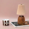 Amber battery operated table lamp with pleated shade styled on books in a cosy home setting.