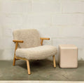 Beige textured armchair with natural wooden legs and armrests styled beside a neutral side table.