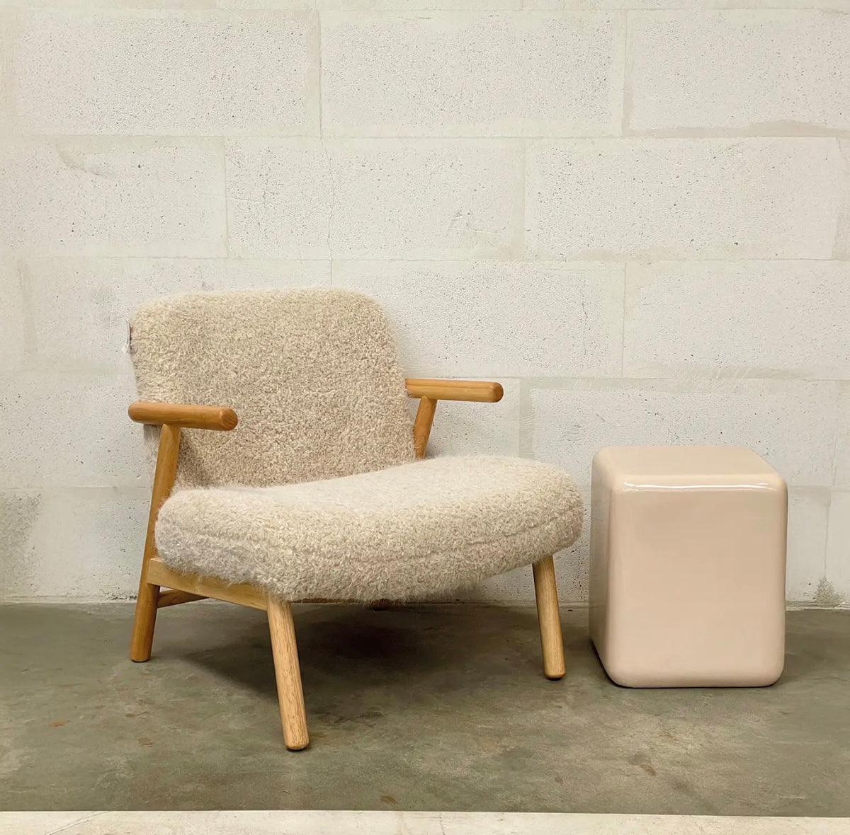 Beige textured armchair with natural wooden legs and armrests styled beside a neutral side table.