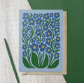 Blue floral greeting card featuring illustrated forget-me-not flowers with green leaves and yellow centres.