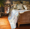 Blue and green patchwork quilted bedspread featuring mixed floral and botanical patterns styled on a traditional bed.