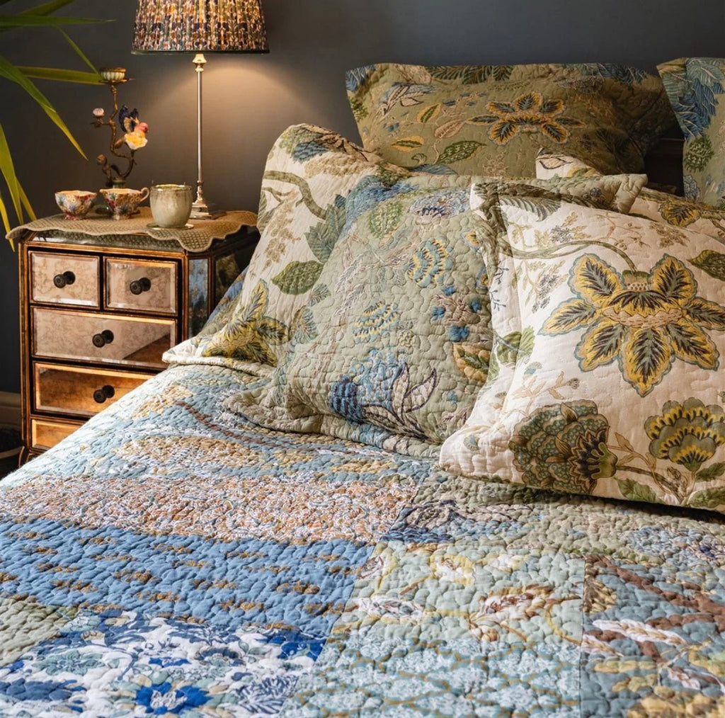 Blue and green patchwork quilted bedspread featuring mixed floral and botanical patterns styled on a traditional bed.