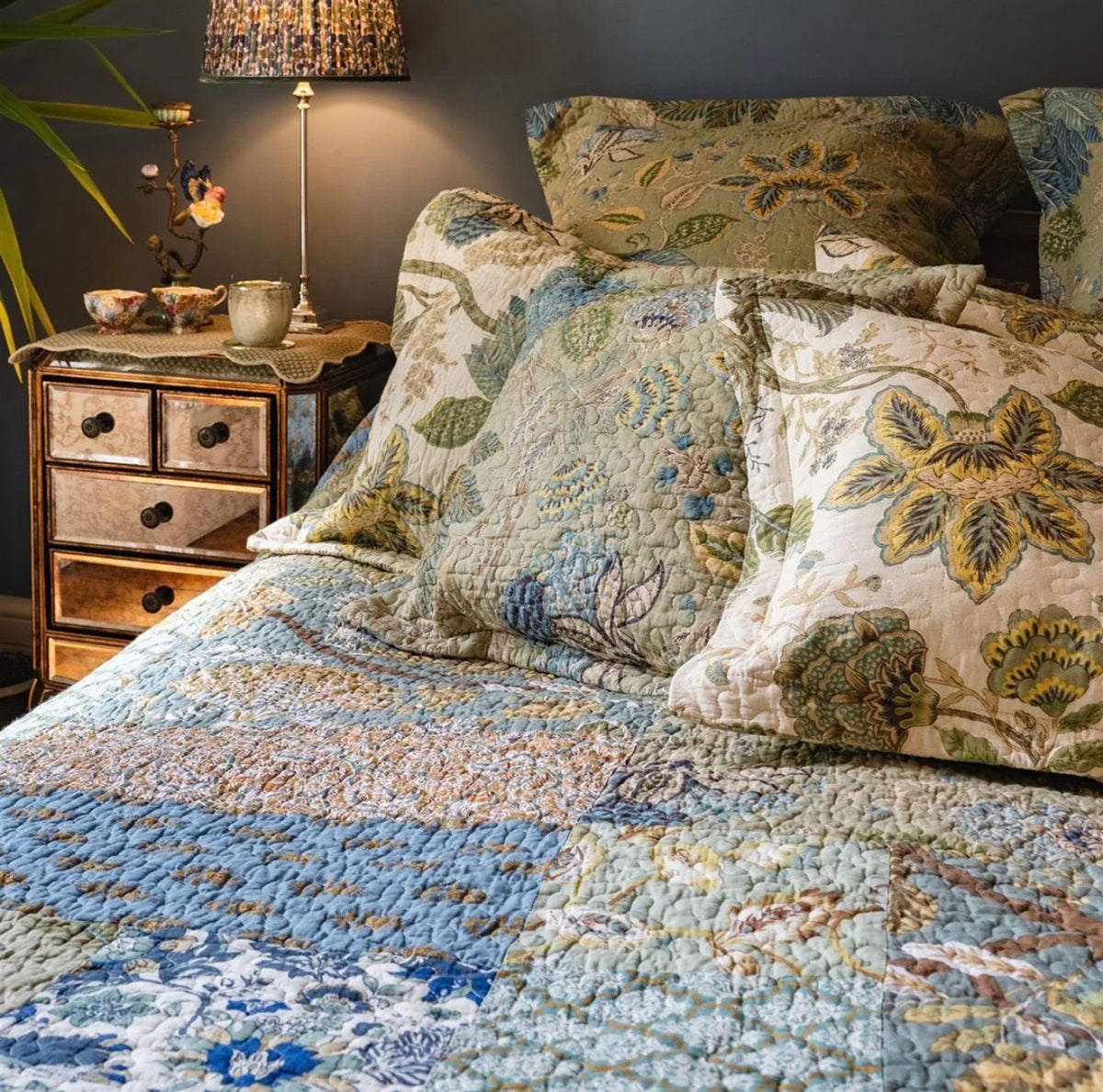 Blue and green patchwork quilted bedspread featuring mixed floral and botanical patterns styled on a traditional bed.