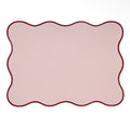 Rectangular blush pink placemat with a wavy scalloped edge and contrasting burgundy border.