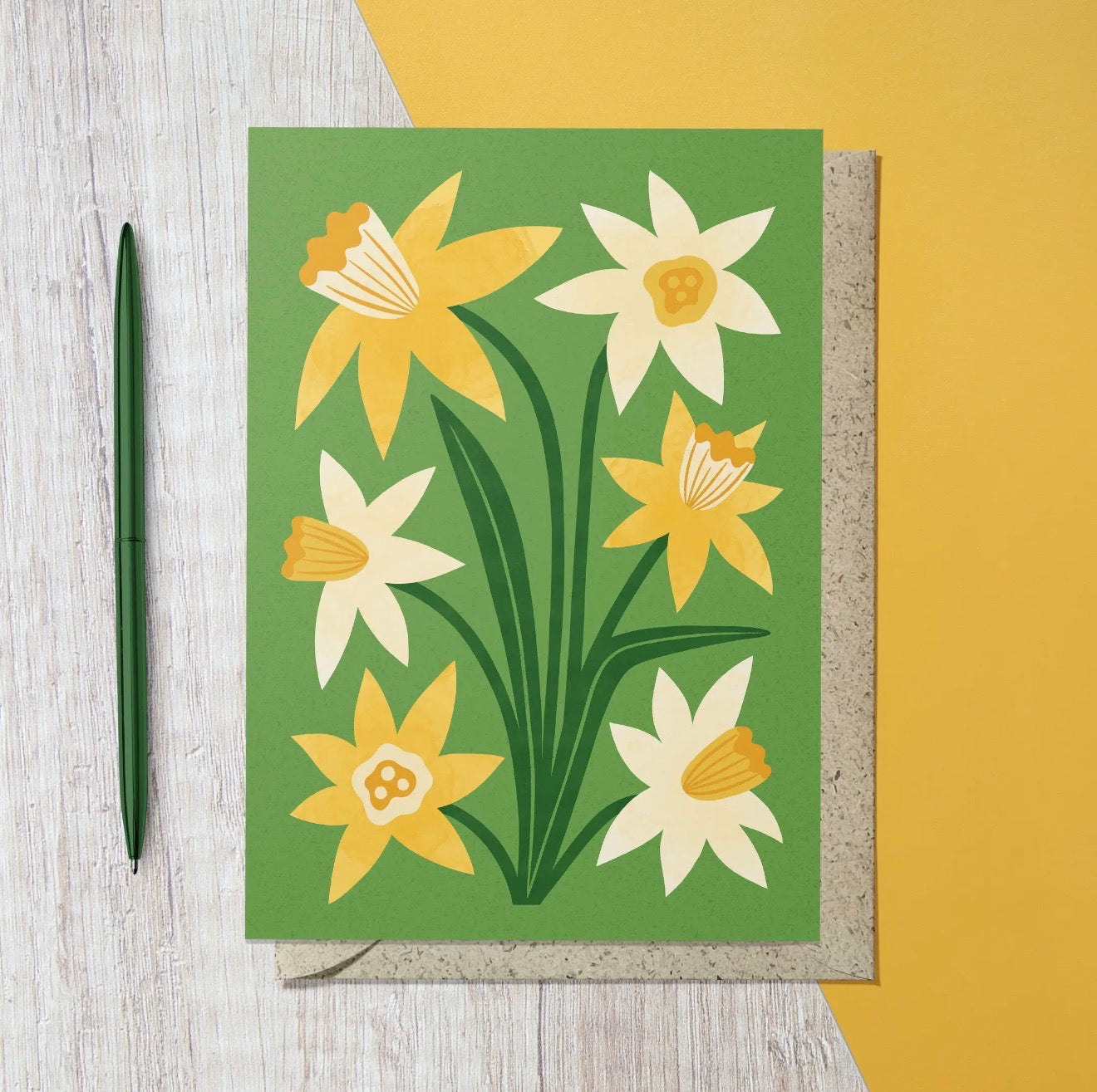 Green greeting card featuring illustrated yellow and cream daffodils with dark green leaves.