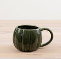 Glossy green pumpkin-shaped ceramic mug with a rounded design and handle, perfect for autumn drinks.
