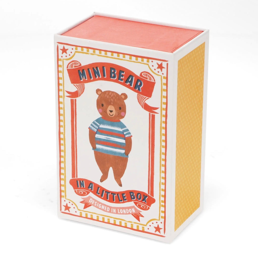 Mini brown bear soft toy wearing a blue striped top tucked into a red and white polka dot bed.
