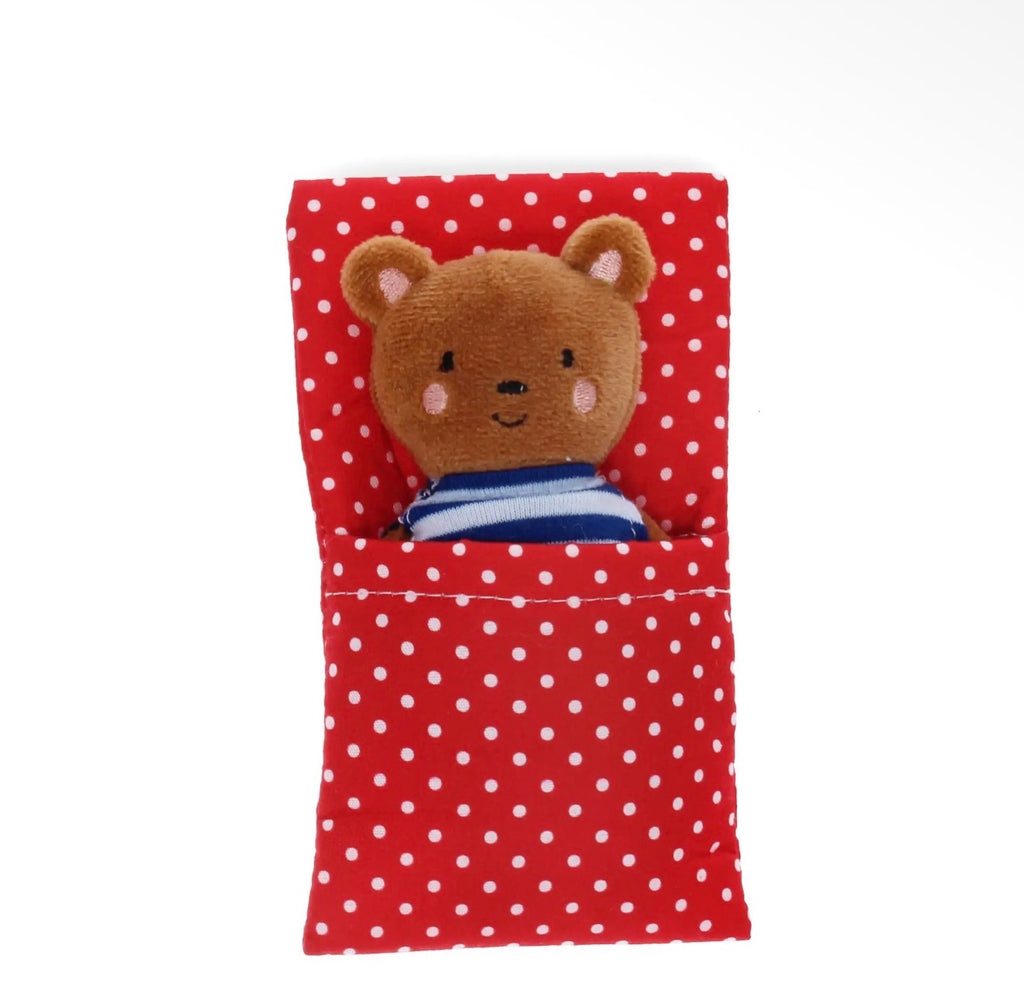 Mini brown bear soft toy wearing a blue striped top tucked into a red and white polka dot bed.