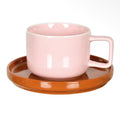 Glossy pale pink cup with a square handle paired with a contrasting warm brown saucer.
