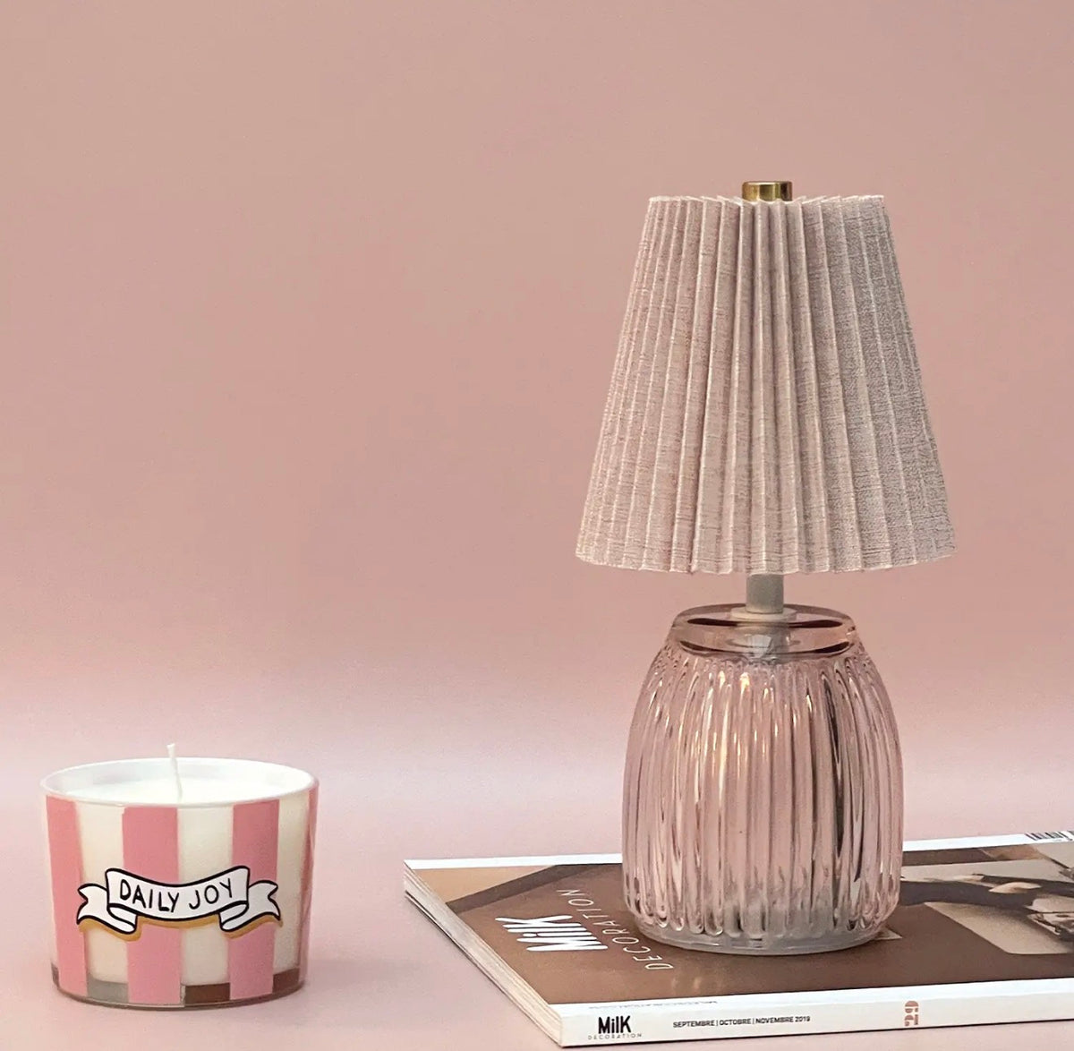 Pink battery operated table lamp styled on books beside a pink striped candle.
