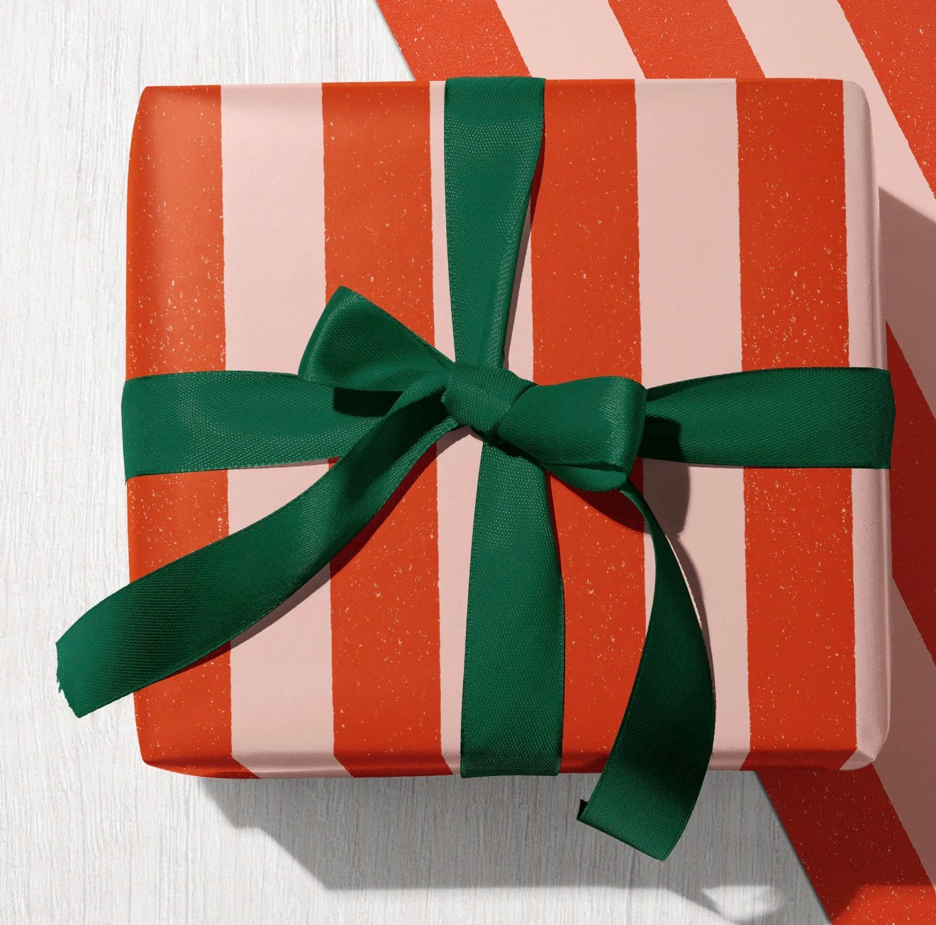 Red and pale pink candy stripe wrapping paper finished with a dark green ribbon bow.