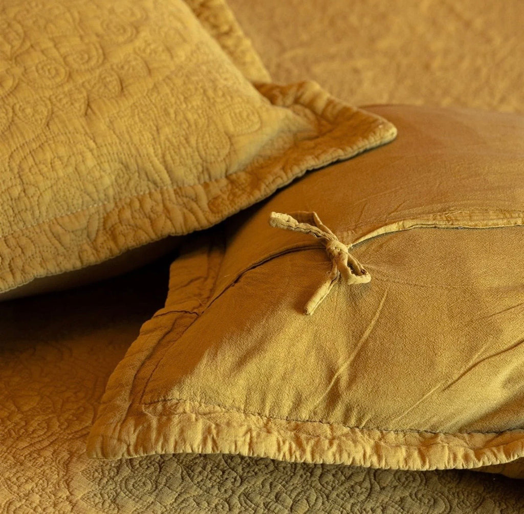 Mustard stonewashed cotton bedspread with an intricate quilted pattern styled on a bed with coordinating cushions.