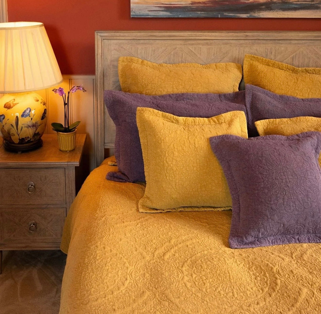 Mustard stonewashed cotton bedspread with an intricate quilted pattern styled on a bed with coordinating cushions.