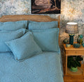 Teal blue quilted continental pillow sham with an intricate stitched pattern styled on a coordinating bed.