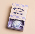 Ceramic oyster keepsake token presented in a pastel matchbox with the message “The World Is Your Oyster”.