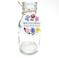 Clear vintage-style glass milk bottle vase with a colourful wildflower illustrated tag tied around the neck.